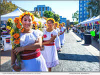 Young women in traditional costumes bring marigolds to adorn altars created in honor of the dead